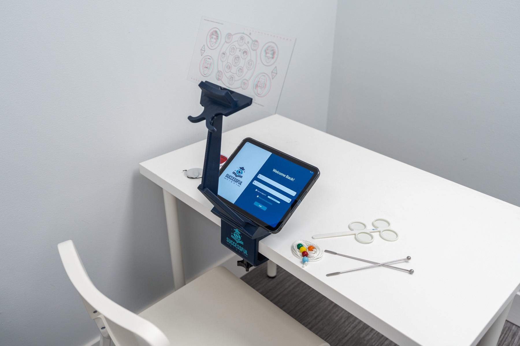 The SuccessfulSight™ therapy stand holding an iPad at the program login, set up on a home desk with a Brock string, lens flippers, and fixation sticks