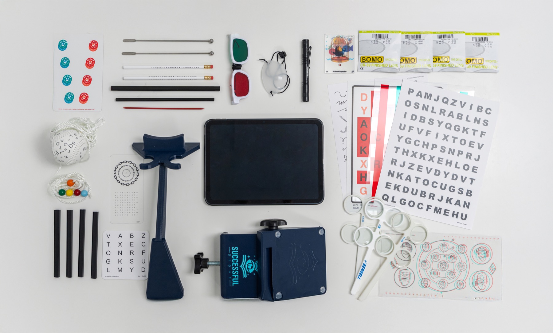 The complete SuccessfulSight™ home equipment kit laid out flat: iPad, branded therapy stand, red-green anaglyph glasses, eye patch, penlight, Brock string, lens flippers, prescription lenses, fixation sticks, and letter and fixation charts
